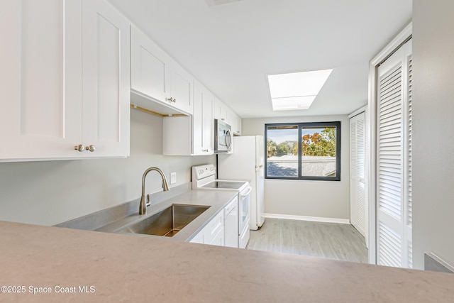 kitchen featuring a skylight, white cabinetry, sink, light hardwood / wood-style flooring, and white appliances