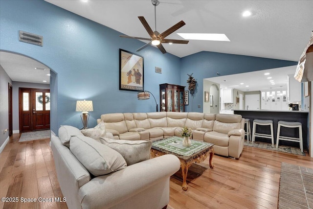 living room with lofted ceiling with skylight, ceiling fan, a textured ceiling, and light wood-type flooring