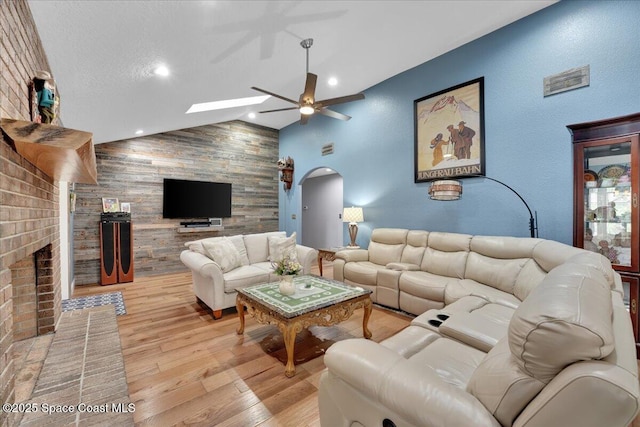 living room with vaulted ceiling, ceiling fan, a textured ceiling, a fireplace, and light hardwood / wood-style floors