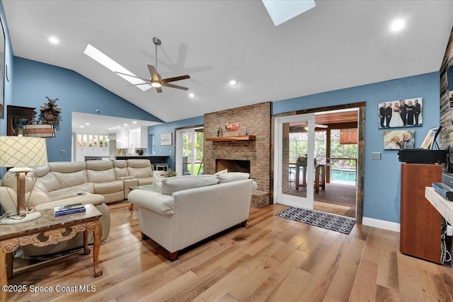 living room featuring a fireplace, ceiling fan, vaulted ceiling with skylight, and light wood-type flooring