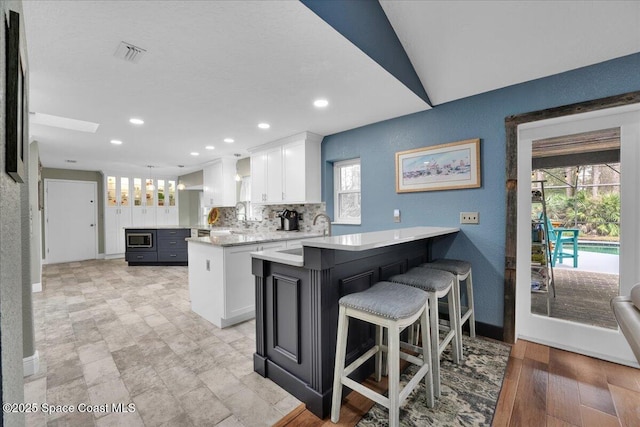 kitchen with stainless steel microwave, a kitchen breakfast bar, kitchen peninsula, a kitchen island, and white cabinetry