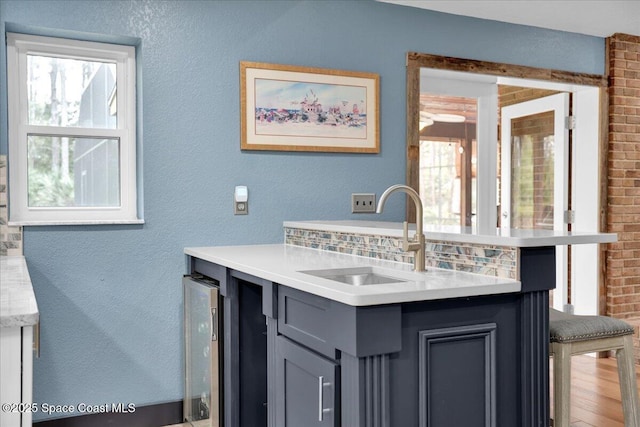 interior space with tasteful backsplash, gray cabinets, sink, and beverage cooler