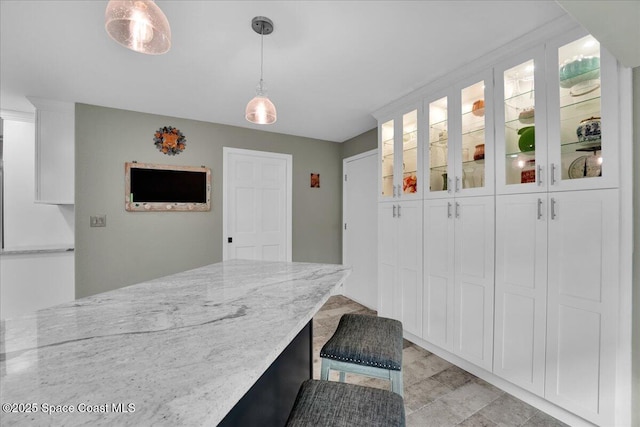 kitchen featuring light stone countertops, white cabinetry, hanging light fixtures, and a kitchen breakfast bar