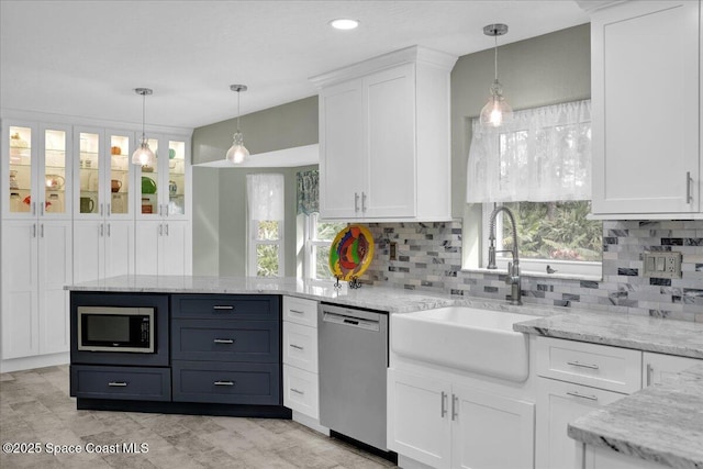 kitchen with light stone countertops, stainless steel appliances, sink, white cabinets, and hanging light fixtures