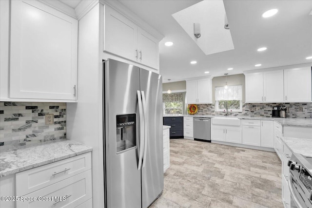 kitchen with decorative backsplash, light stone counters, stainless steel appliances, sink, and white cabinetry