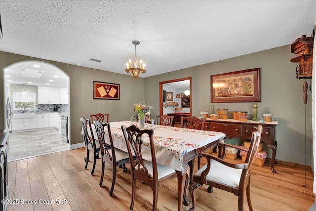 dining room with an inviting chandelier, a textured ceiling, and light wood-type flooring