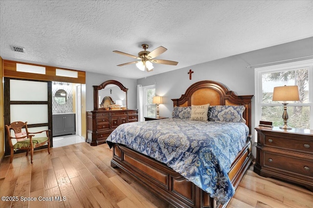 bedroom featuring ceiling fan, ensuite bathroom, a textured ceiling, and light wood-type flooring