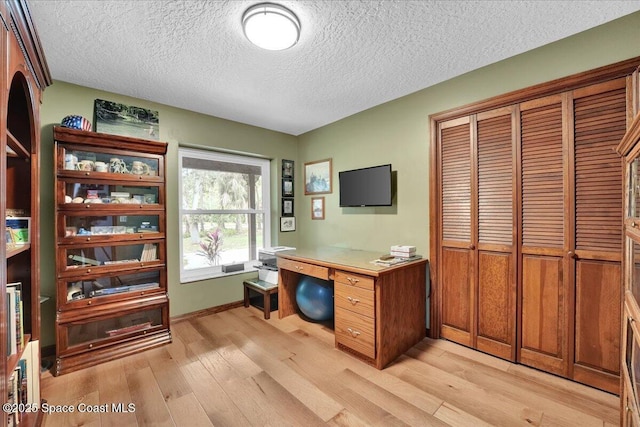 home office featuring light wood-type flooring and a textured ceiling