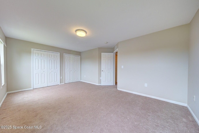 unfurnished bedroom featuring carpet, baseboards, and multiple closets