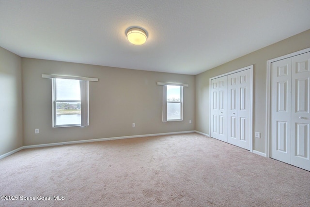 unfurnished bedroom with carpet floors, multiple windows, baseboards, and two closets