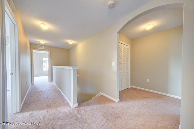 hall featuring arched walkways, a textured ceiling, an upstairs landing, baseboards, and carpet