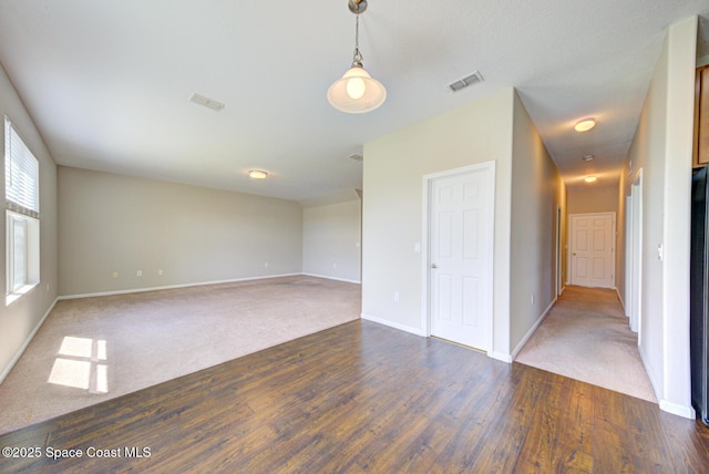 unfurnished room with dark colored carpet, dark wood finished floors, visible vents, and baseboards