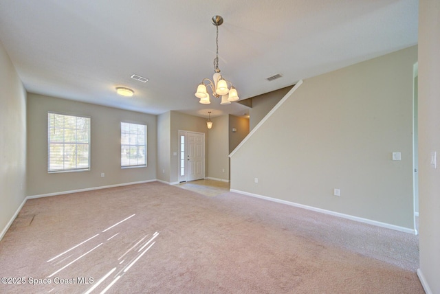 empty room with carpet floors, an inviting chandelier, visible vents, and baseboards