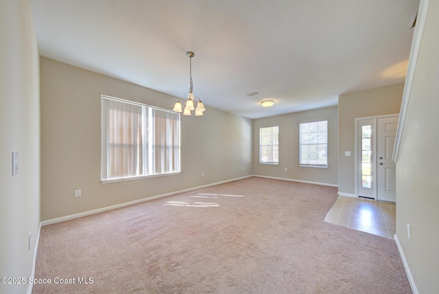 carpeted empty room featuring baseboards and a notable chandelier