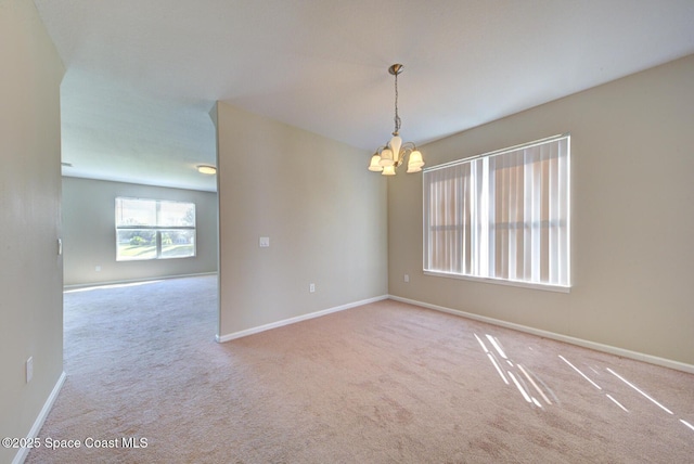 carpeted empty room featuring baseboards and a chandelier