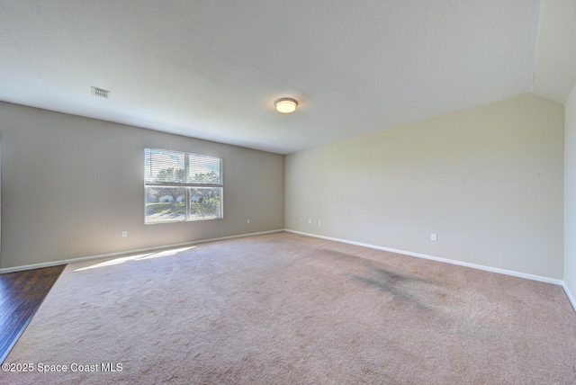 carpeted spare room with vaulted ceiling, a textured ceiling, visible vents, and baseboards