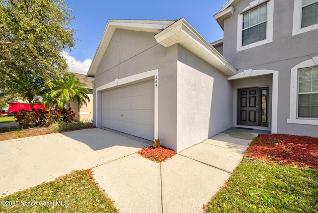 doorway to property featuring an attached garage, concrete driveway, and stucco siding