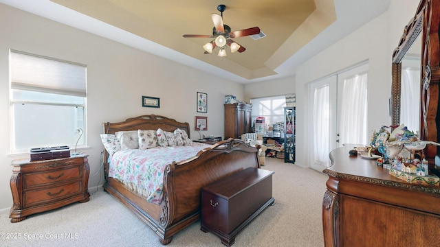 bedroom with a tray ceiling, ceiling fan, french doors, and light carpet