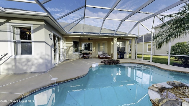 view of pool with glass enclosure, ceiling fan, area for grilling, and a patio