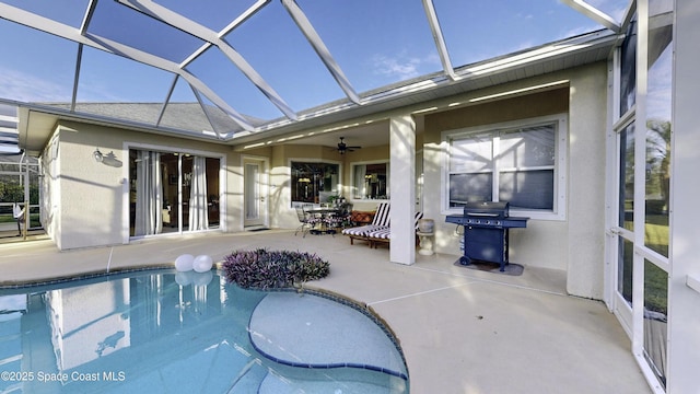 view of pool with ceiling fan, area for grilling, a patio, and glass enclosure