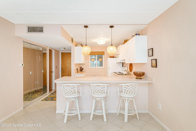 kitchen featuring pendant lighting, a breakfast bar area, white refrigerator, white cabinets, and kitchen peninsula