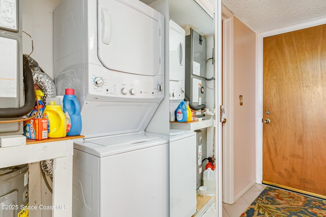 laundry area featuring stacked washer and dryer, light tile patterned floors, and a textured ceiling