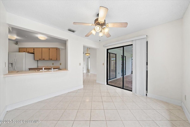 unfurnished living room featuring ceiling fan, sink, light tile patterned floors, and a textured ceiling