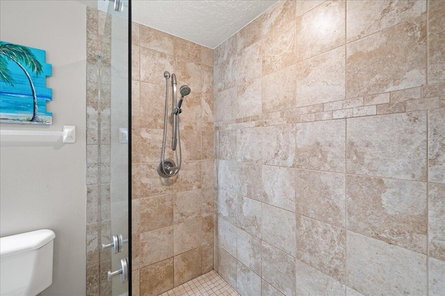 bathroom with a tile shower, toilet, and a textured ceiling