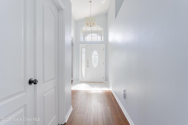 entryway with wood-type flooring, an inviting chandelier, and lofted ceiling