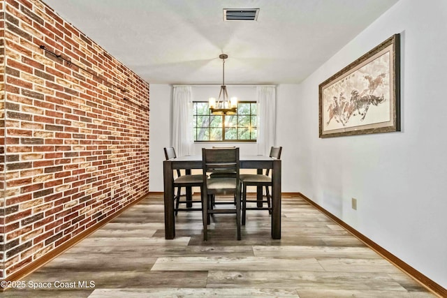 dining room with light hardwood / wood-style flooring, brick wall, and an inviting chandelier