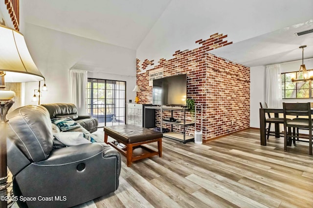 living room with high vaulted ceiling, light hardwood / wood-style flooring, a notable chandelier, and brick wall