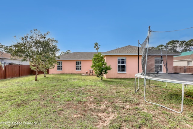 rear view of property featuring a yard and a trampoline