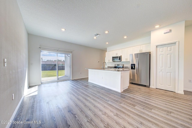 kitchen featuring an island with sink, white cabinets, stainless steel appliances, and light hardwood / wood-style floors