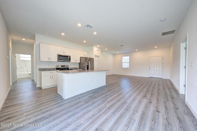 kitchen featuring stone counters, stainless steel appliances, light hardwood / wood-style floors, a kitchen island with sink, and white cabinets