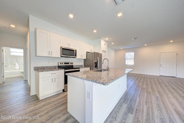 kitchen featuring white cabinets, appliances with stainless steel finishes, a center island with sink, and sink