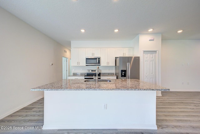 kitchen with sink, light stone counters, a center island with sink, white cabinets, and appliances with stainless steel finishes