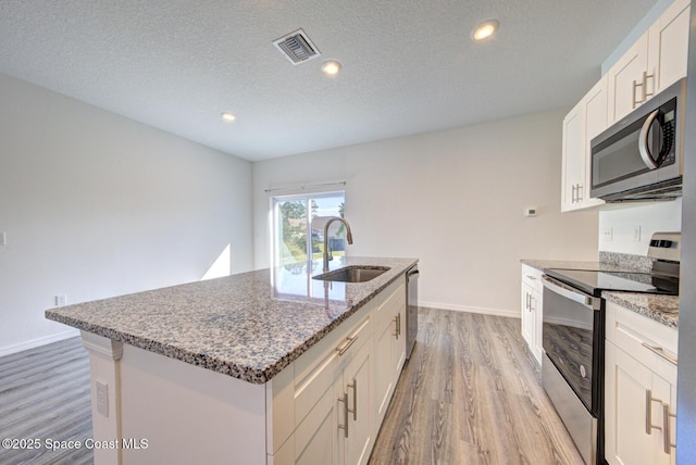 kitchen featuring a center island with sink, sink, a textured ceiling, appliances with stainless steel finishes, and white cabinetry