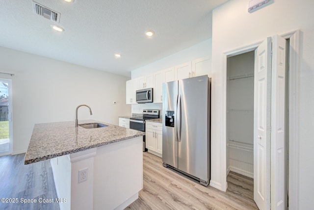 kitchen featuring light stone counters, stainless steel appliances, sink, white cabinetry, and an island with sink