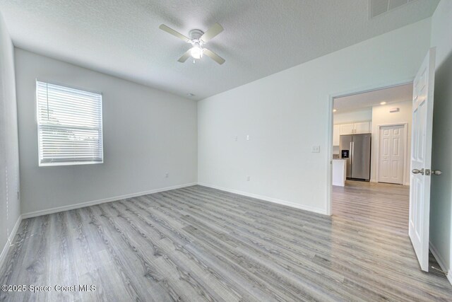 spare room with a textured ceiling, light wood-type flooring, and ceiling fan