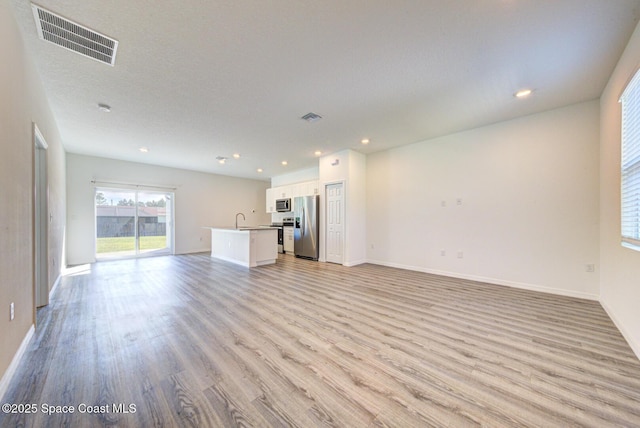 unfurnished living room with a textured ceiling, light wood-type flooring, and sink