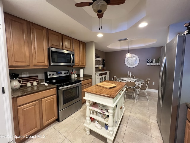 kitchen featuring a tray ceiling, butcher block countertops, light tile patterned floors, and appliances with stainless steel finishes