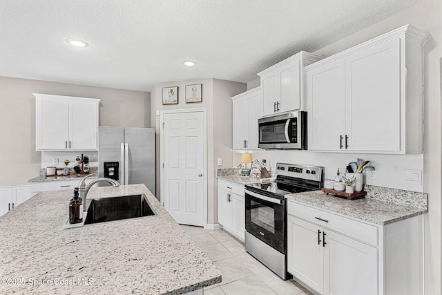 kitchen featuring sink, light tile patterned floors, a textured ceiling, white cabinets, and appliances with stainless steel finishes