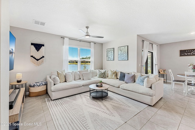 tiled living room featuring a textured ceiling, a water view, and ceiling fan