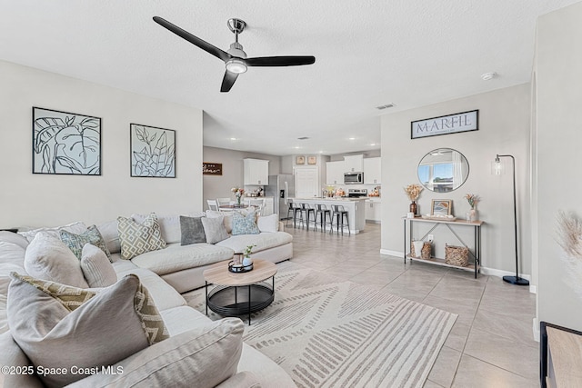 living room with ceiling fan, light tile patterned flooring, and a textured ceiling