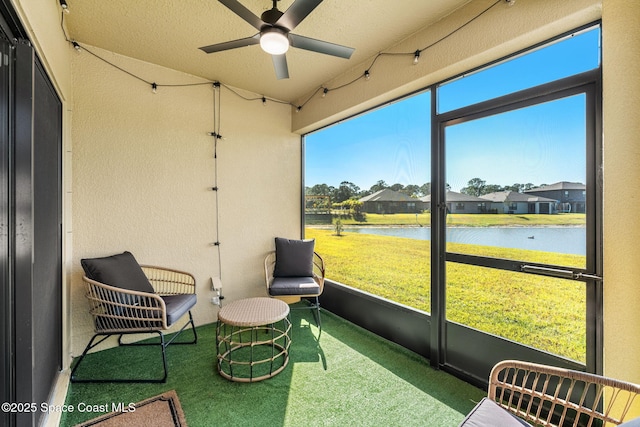 sunroom with ceiling fan and a water view