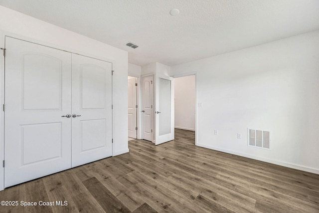 unfurnished bedroom with a textured ceiling, dark hardwood / wood-style flooring, and a closet