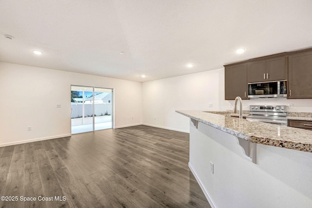 kitchen featuring dark brown cabinetry, light stone counters, dark hardwood / wood-style flooring, a breakfast bar, and appliances with stainless steel finishes