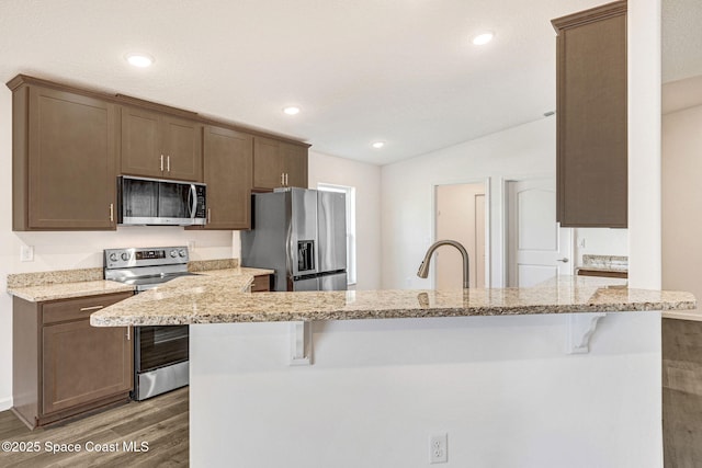 kitchen featuring dark wood-type flooring, light stone counters, kitchen peninsula, a breakfast bar area, and appliances with stainless steel finishes