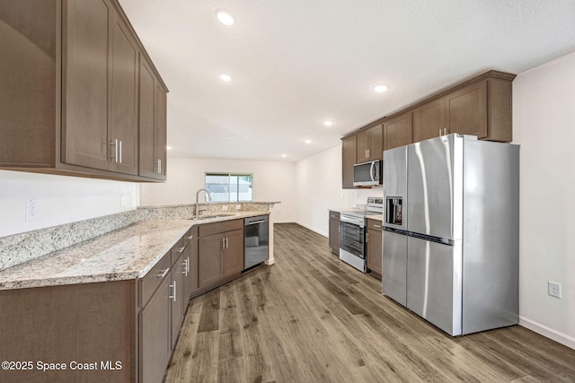 kitchen featuring hardwood / wood-style floors, sink, appliances with stainless steel finishes, light stone counters, and kitchen peninsula