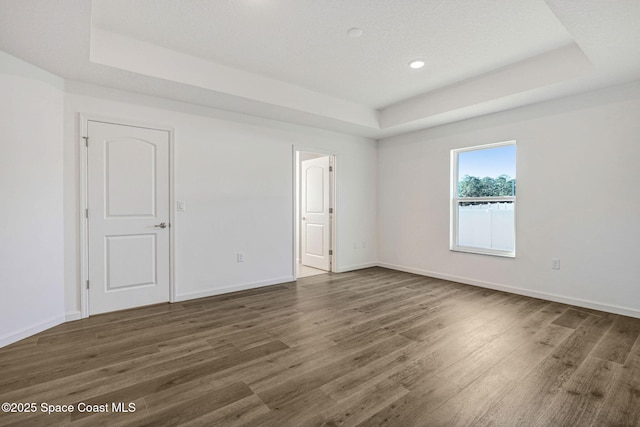 empty room with dark wood-type flooring and a tray ceiling